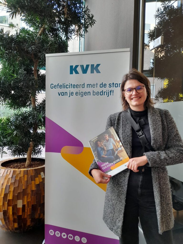Jonge vrouw met bril lacht in de camera. Ze heeft een map in haar hand.